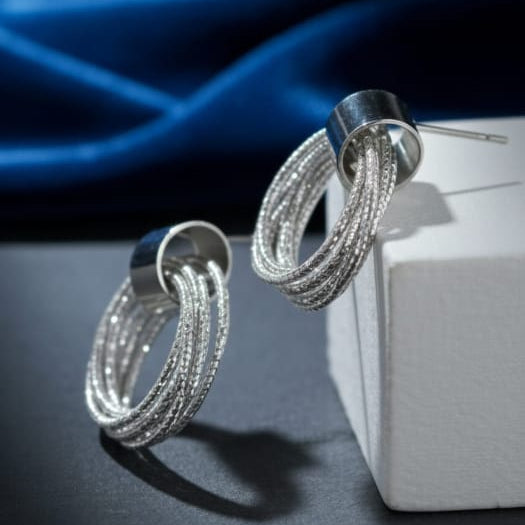 Silver hoop earrings on a dark surface with a blue fabric background